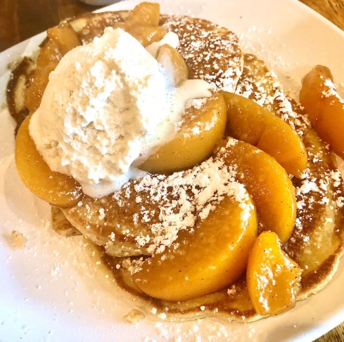 Fluffy pancakes topped with sliced peaches and a dollop of whipped cream, dusted with powdered sugar.