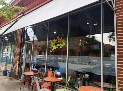 Exterior view of a restaurant with large windows, featuring colorful signage and outdoor seating.