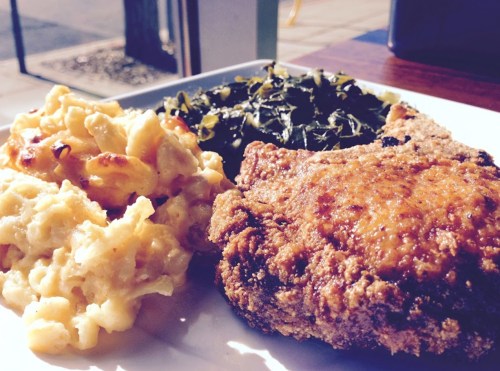 A plate of fried chicken, macaroni and cheese, and collard greens, served on a white dish in natural light.