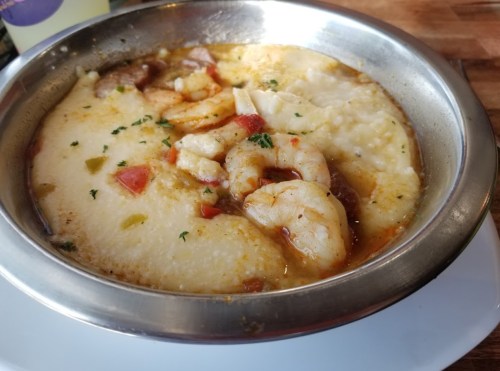 A bowl of creamy shrimp and grits topped with herbs and diced vegetables.