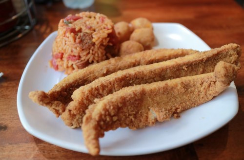 A plate with three pieces of fried fish, a serving of rice, and small fried balls on the side.