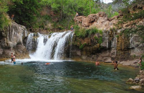 A scenic waterfall cascades into a clear pool, with people swimming and enjoying the natural surroundings.