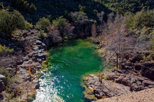 A serene green pool surrounded by rocky terrain and sparse trees under a clear blue sky.