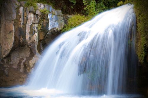 A serene waterfall cascading over rocky cliffs, surrounded by lush greenery.