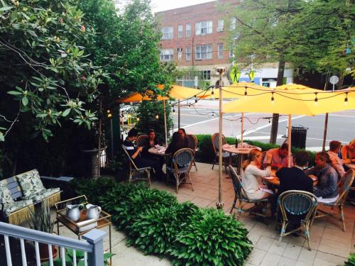 Outdoor dining area with orange umbrellas, tables, and greenery, featuring people enjoying meals in a lively setting.