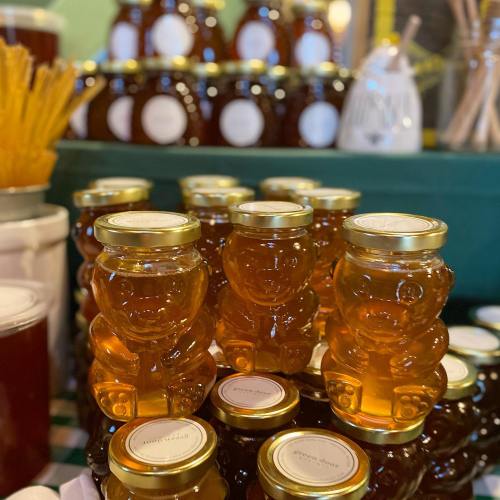 A display of honey jars shaped like bears, with more jars in the background, all on a green table.