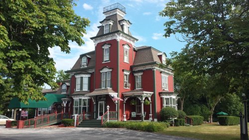 Victorian-style red house with a tower, surrounded by greenery and a blue sky.