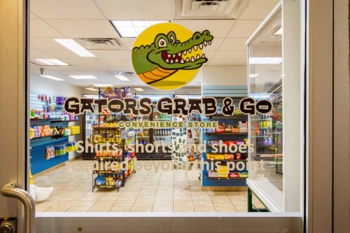Storefront of Gators Grab & Go convenience store, featuring colorful displays of snacks and merchandise inside.