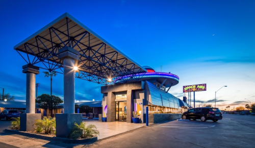 A modern diner with a futuristic design, featuring a large overhang and colorful neon lights at dusk.