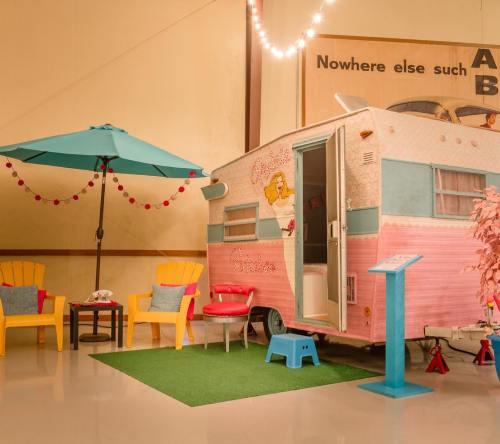 A vintage pink and blue trailer with outdoor seating, an umbrella, and decorative lights in a cozy indoor setting.