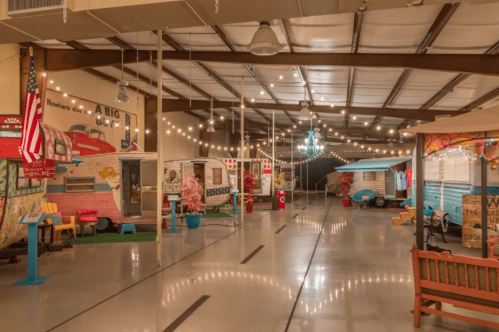 A colorful indoor space featuring vintage trailers, string lights, and decorative elements, creating a cozy atmosphere.