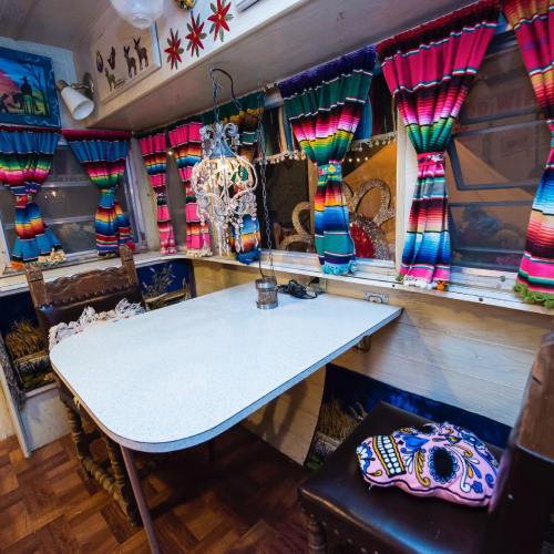 Colorful interior of a vintage trailer with vibrant curtains, a decorative chandelier, and a table set for dining.