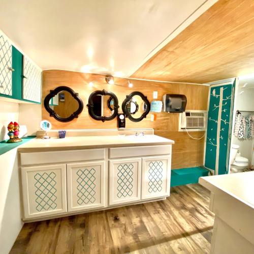 Bright bathroom with wooden accents, teal decor, mirrors, and a sink area. Features an air conditioner and a toilet in the background.