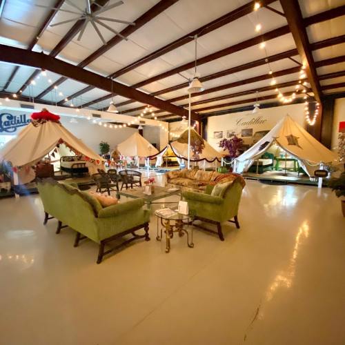 A cozy indoor space with green sofas, decorative tents, and string lights, creating a warm, inviting atmosphere.