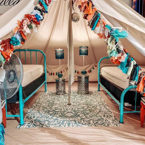 A cozy tent interior with two turquoise beds, decorative lamps, and colorful garlands hanging from the ceiling.