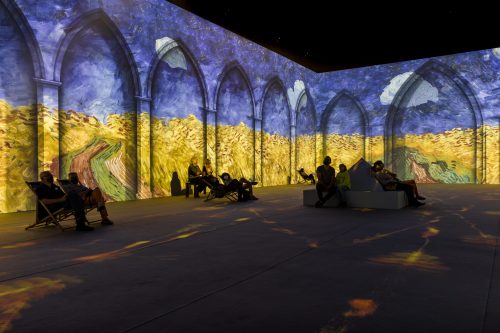 Visitors relax in a dimly lit space with vibrant, projected Van Gogh artwork on the walls.