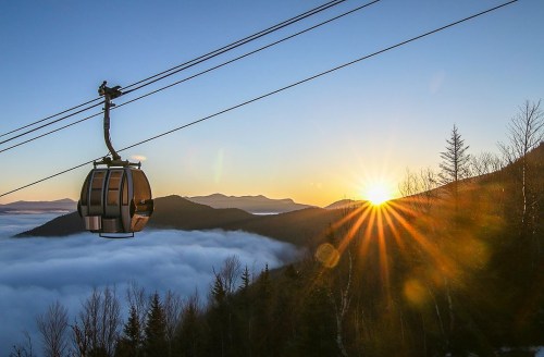 A cable car glides over a sea of clouds at sunrise, with mountains silhouetted in the background.