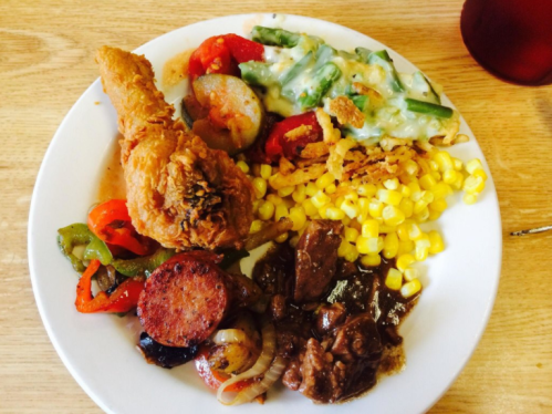 A plate of food featuring fried chicken, sausage, corn, green beans, and mixed vegetables.
