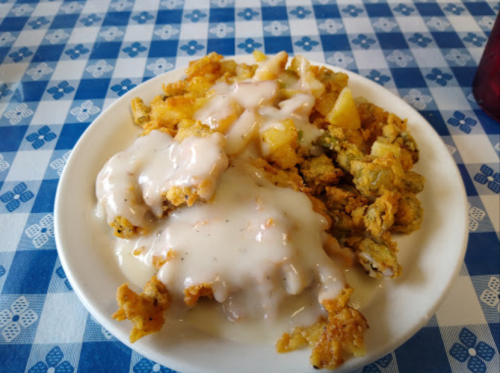 A plate of fried food topped with creamy gravy, served on a blue checkered tablecloth.