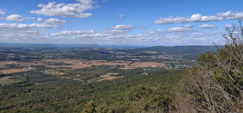 A panoramic view of rolling hills and farmland under a blue sky with fluffy clouds.