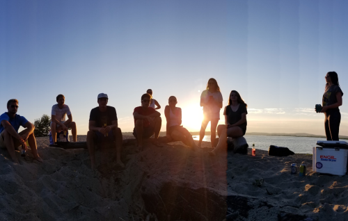 A group of people sitting on a beach at sunset, enjoying each other's company by the water.