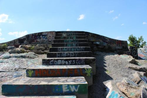 Colorful graffiti covers stone steps leading up to a flat, elevated area under a clear blue sky.