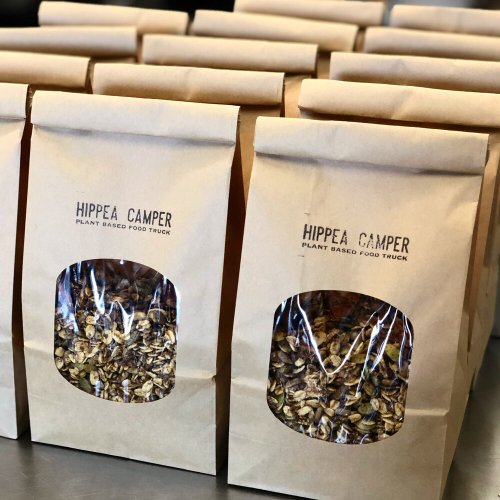 Brown paper bags filled with granola, labeled "HIPPEA CAMPER PLANT BASED FOOD TRUCK," arranged on a table.