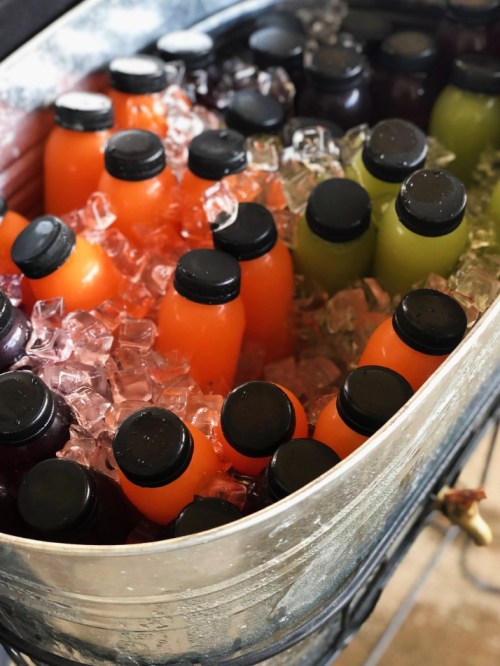 A metal tub filled with ice and various bottles of colorful beverages, including orange, green, and dark purple drinks.