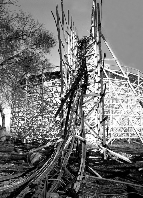 A black and white image of a damaged wooden structure with charred beams and debris scattered around.