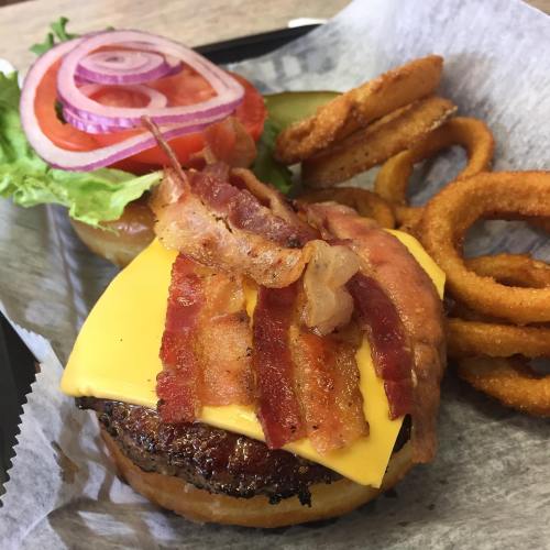 A juicy cheeseburger topped with bacon, served with lettuce, tomato, onion, pickles, and crispy onion rings.