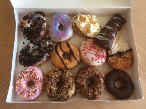 A box of assorted donuts featuring various toppings and flavors, including sprinkles, chocolate, and coconut.