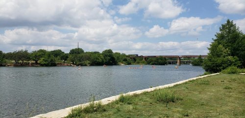 A serene river scene with kayakers, green trees, and a cloudy sky, featuring a bridge in the background.