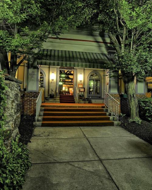 A well-lit entrance to a building with a green awning, surrounded by trees and a stone wall, at night.