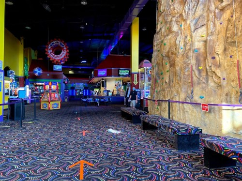 A colorful indoor entertainment center featuring a climbing wall, arcade games, and patterned carpet.