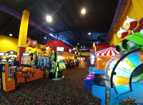 Brightly colored arcade interior with various games, including a large robotic machine and carnival-themed decor.