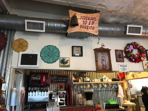 Interior of a cozy restaurant featuring colorful decor, a sign for a "10 lb Burrito," and a coffee station.