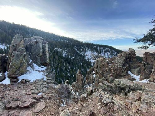 Rocky cliffside overlooking a snow-dusted forested valley under a clear sky.