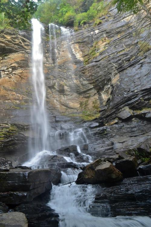 A cascading waterfall flows down rocky cliffs, surrounded by lush greenery and a stream at the base.