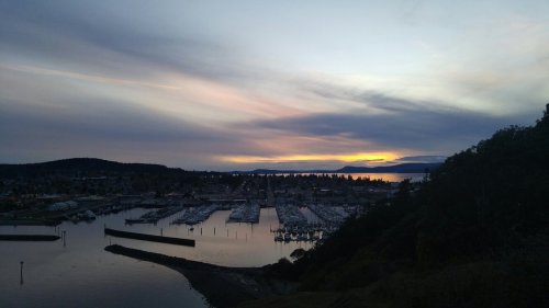 A serene harbor at sunset, with boats docked and colorful clouds reflecting on the water.