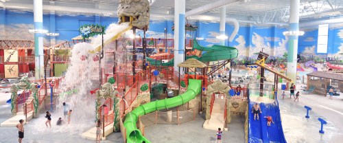 A vibrant indoor water park featuring slides, a large water feature, and families enjoying the attractions.