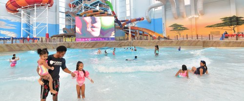 A family enjoys a water park with slides, a large screen, and children playing in the wave pool.
