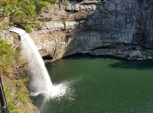 A waterfall cascades into a deep green pool surrounded by rocky cliffs and lush vegetation.