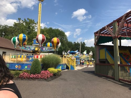 Colorful amusement park rides with hot air balloon designs, surrounded by greenery and flowers under a blue sky.