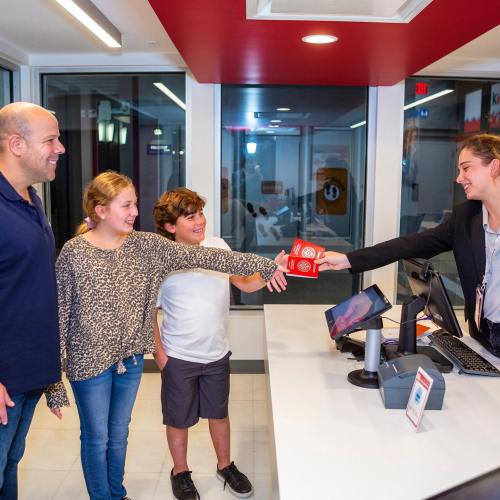A family at a counter receiving tickets from a smiling employee in a modern setting.