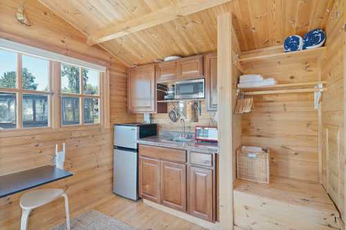 Cozy wooden cabin interior featuring a kitchenette with a fridge, microwave, and storage shelves.