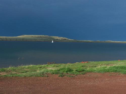 A calm lake under a dark sky, with a small sailboat in the distance and green grass along the shore.
