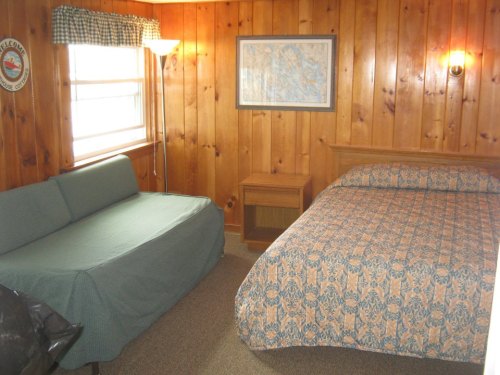 Cozy room with wooden walls, a bed with patterned bedding, a green couch, and a small nightstand.