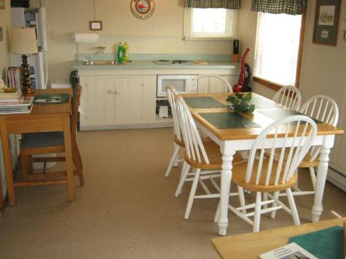 A cozy kitchen with a wooden dining table, chairs, and a small cooking area, featuring light-colored cabinets and natural light.