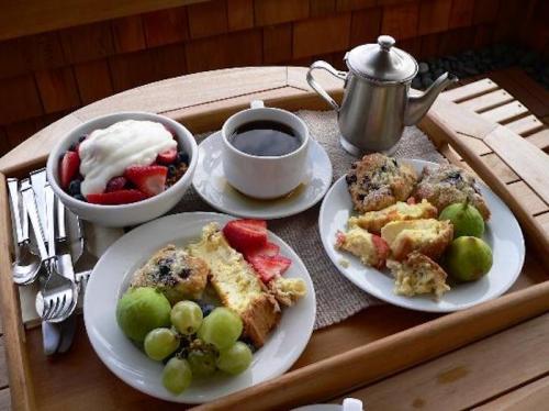 A wooden tray with two plates of breakfast, including fruit, baked goods, yogurt, and a cup of coffee.