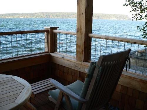 A wooden deck with a rocking chair overlooks a serene lake and distant trees under a clear sky.